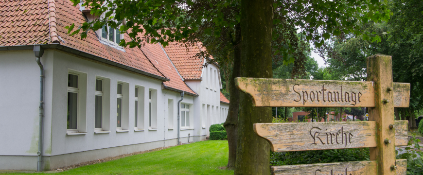 Gebäude mit Wegweiser zu Sportanlage, Kirche und Schule